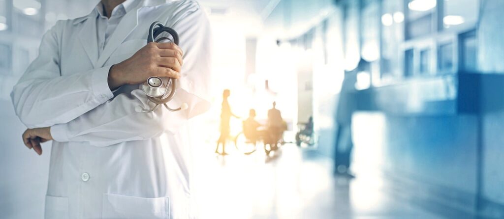 A doctor stands holding a stethoscope against a hospital corridor background representing data discovery and electronic personal health information for healthcare providers